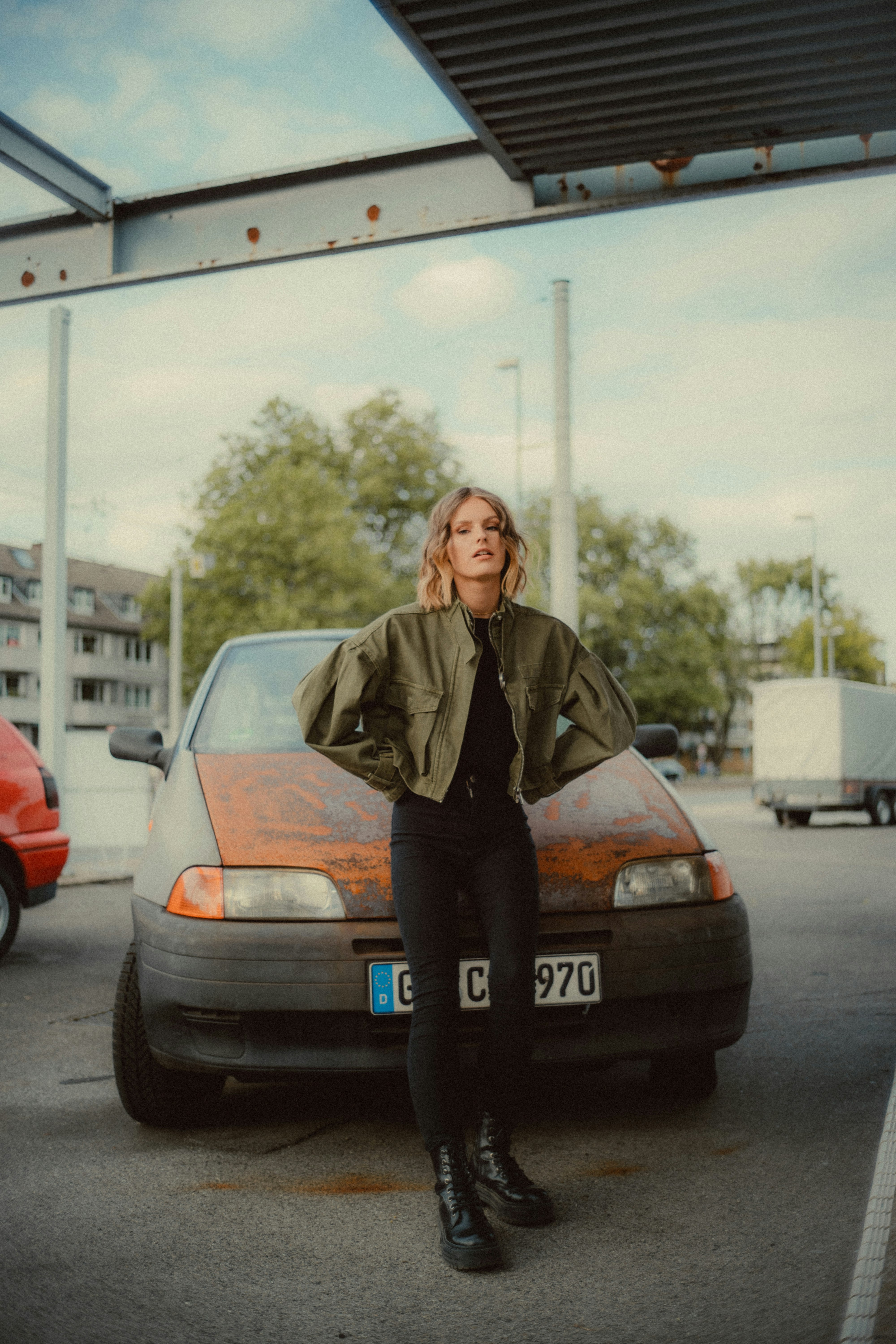 woman in brown jacket standing beside blue car during daytime